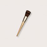 Make-up-Pinsel mit Holzgriff und dicht gepackten, dunklen Borsten. Der Pinsel hat eine konische, abgewinkelte Form, die sich zum Konturieren oder zum Auftragen von Rouge eignet. Er befindet sich auf einem hellen, neutralen Hintergrund.