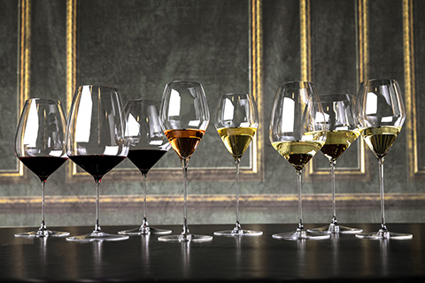 Eine Reihe verschiedener Weingläser auf einer dunklen Oberfläche, jedes mit unterschiedlichen Weinsorten gefüllt, darunter Rot-, Weiß- und Roséwein. Der Hintergrund zeigt eine elegante, strukturierte Wand mit goldenen Akzenten.