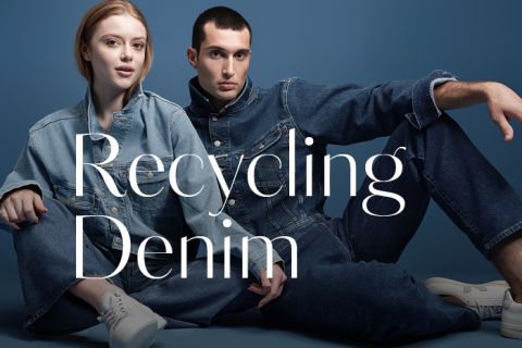 Zwei Models posieren vor einem blauen Hintergrund und tragen Jeans in verschiedenen Farbtönen. Der Text auf dem Bild lautet „Recycling Denim“. Das männliche Model hat kurze Haare und das weibliche Model hat lange Haare. Beide sitzen lässig da.