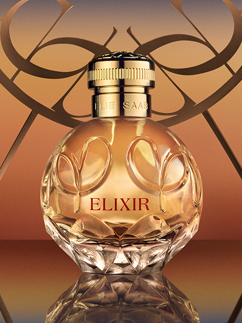 Ein gläserner Parfümflakon mit der Aufschrift „Elie Saab Elixir“ und einem goldenen Verschluss steht vor einem warmen Hintergrund mit Farbverlauf. Der runde Flakon ist mit dekorativen Blumengravuren versehen und reflektiert das Licht, wodurch er ein elegantes und luxuriöses Aussehen erhält.