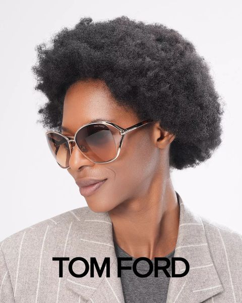 Person mit kurzer Afrofrisur, die eine große Sonnenbrille und einen grauen Nadelstreifenblazer trägt. Auf dem Bild steht unten „Tom Ford“. Der Hintergrund ist schlicht weiß.