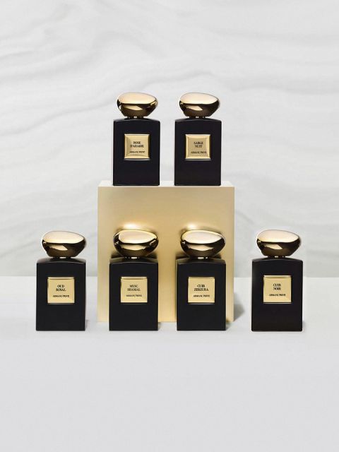 Es werden sechs elegante Parfümflakons mit glatten, goldfarbenen Verschlüssen ausgestellt. Sie sind auf und um einen Goldblock angeordnet und tragen verschiedene Etiketten mit den Aufschriften „OUD“, „SNAKE“ und „OUR“, die jeweils kunstvolle schwarz-goldene Muster auf einem sanften grauen Hintergrund aufweisen.