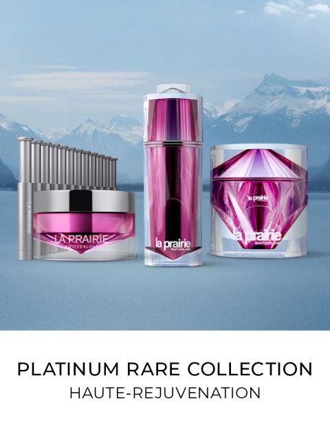 Eine Kollektion von La Prairie Platinum Rare Hautpflegeprodukten, darunter eine Creme, ein Serum und ein Applikator. Sie haben eine elegante lila- und silberfarbene Verpackung vor einer Kulisse aus schneebedeckten Bergen und einem See. Text: „Platinum Rare Collection, Haute-Rejuvenation.