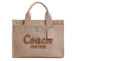 Beigefarbene Coach-Tragetasche mit aufgesticktem „Coach New York“ auf der Vorderseite. Die Tasche hat zwei kurze Griffe und ein daran befestigtes Gepäcketikett. Der Hintergrund ist weiß.