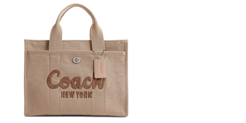 Beigefarbene Coach-Tragetasche mit aufgesticktem „Coach New York“ auf der Vorderseite. Die Tasche hat zwei kurze Griffe und ein daran befestigtes Gepäcketikett. Der Hintergrund ist weiß.