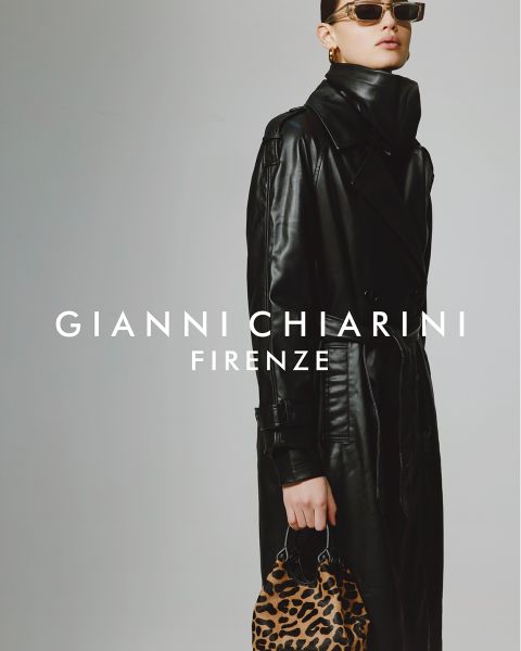 Person, die einen langen schwarzen Trenchcoat aus Leder und eine Sonnenbrille trägt und eine kleine Tasche mit Leopardenmuster hält. Der Hintergrund ist grau, mit dem Text „GIANNI CHIARINI FIRENZE“ in Weiß über dem Bild.