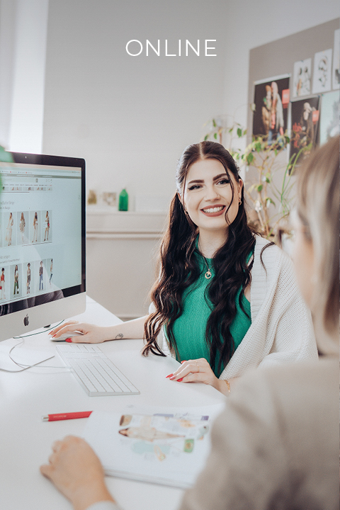 Eine Frau mit langem dunklem Haar, die ein grünes Oberteil und eine weiße Strickjacke trägt, lächelt, während sie an einem Computer arbeitet. Der Bildschirm zeigt Bilder. Im Vordergrund ist eine weitere Person zu sehen, unscharf. Der Text oben lautet „ONLINE“.