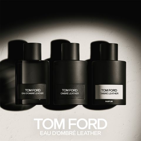 Drei schwarze Flakons mit Tom Ford-Parfums mit den Aufschriften „Eau d'Ombre Leather“, „Ombre Leather“ und „Parfum“ stehen aufgereiht. Sie werfen Schatten auf eine helle Oberfläche, darunter steht fettgedruckt „TOM FORD EAU D'OMBRE LEATHER“.