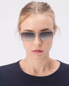 Eine Person mit hellbraunem Haar trägt eine rechteckige Sonnenbrille und ein marineblaues Oberteil und steht vor einem schlichten weißen Hintergrund.