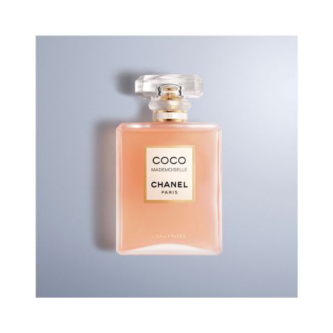 Eine Flasche Chanel Coco Mademoiselle L'Eau Privée Parfüm auf hellblauem Hintergrund. Die Flasche ist rosa mit einem goldenen Etikett und einem klaren, quadratischen Verschluss.