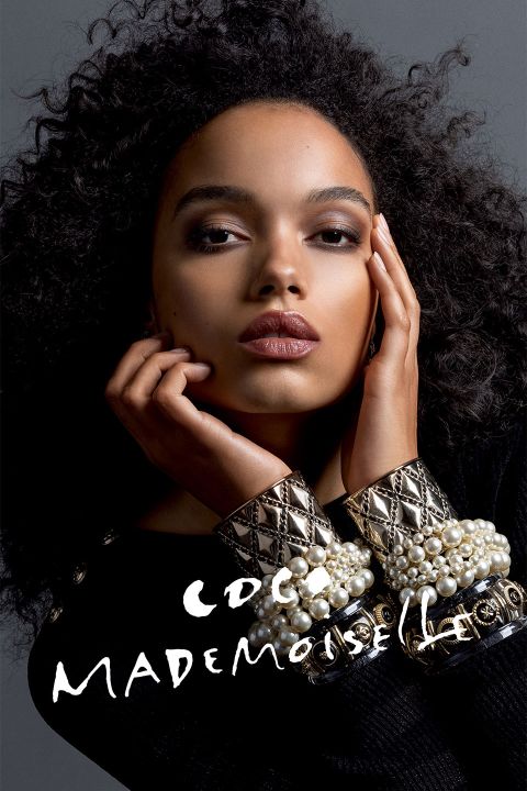 Eine Frau mit lockigem Haar posiert mit den Händen vor dem Gesicht und präsentiert aufwendigen Schmuck und ein schwarzes Outfit. Der Text „COCO MADEMOISELLE“ steht in weißer Schrift am unteren Bildrand.