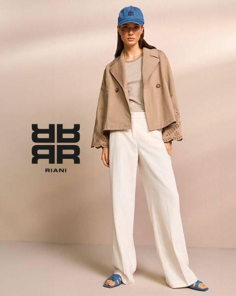 Ein Model trägt eine hellbraune Jacke mit Spitzenärmeln, ein gestreiftes Oberteil und weiße Hosen mit weitem Bein. Dazu trägt sie eine blaue Mütze und Sandalen. Das Riani-Logo und der Name erscheinen auf der linken Seite des Bildes vor einem neutralen Hintergrund.