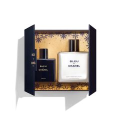 Offene Schachtel mit zwei Flaschen Bleu de Chanel: links eine Parfümflasche und rechts eine Flasche feuchtigkeitsspendende Hautpflege. Der Hintergrund hat ein kunstvolles Goldmuster. Die Schachtel ist dunkel mit goldenen Details.