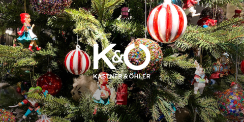 Ein Weihnachtsbaum, der mit farbenfrohen Ornamenten geschmückt ist, darunter rot-weiß gestreifte Kugeln und verschiedene Figuren. Das Logo „Kastner & Öhler“ ist zentriert über dem Baum angebracht.