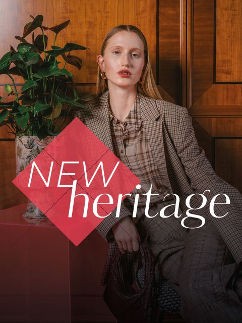 Eine Frau in einem karierten Anzug sitzt neben einer Pflanze, vor ihr ist der Schriftzug „NEW heritage“ eingeblendet.