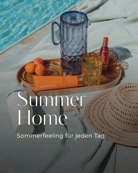 Eine Szene am Pool mit einem Strohhut, Sonnencreme, Aprikosen, einem Glaskrug, Getränken und einem Tablett. Der Text lautet: "Summer Home - Sommerfeeling für jeden Tag.