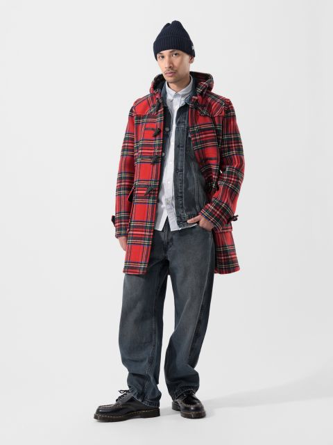 Eine Person, die einen roten Karomantel, eine Jeansjacke, ein weißes Hemd, weite Jeans, schwarze Schuhe und eine dunkle Strickmütze trägt, steht vor einem schlichten weißen Hintergrund.