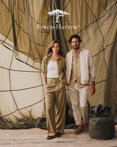 Ein Mann mit gewelltem braunem Haar und Bart trägt einen marineblauen Pullover und steht vor einer beigefarbenen, strukturierten Wand. Das Logo und der Name von Fynch-Hatton erscheinen in der oberen rechten Ecke.