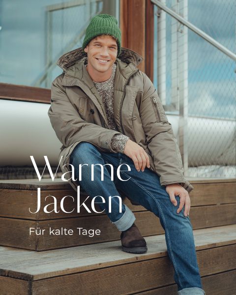 Ein lächelnder Mann mit grüner Strickmütze, beiger Winterjacke, Jeans und braunen Stiefeln sitzt auf einer Holztreppe im Freien. Der Text lautet: "Wärme Jacken. Für kalte Tage.