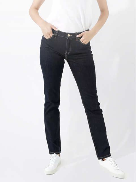 Eine Person, die ein weißes T-Shirt, dunkelblaue Jeans und weiße Turnschuhe trägt, steht mit den Händen in den Taschen vor einem schlichten weißen Hintergrund.
