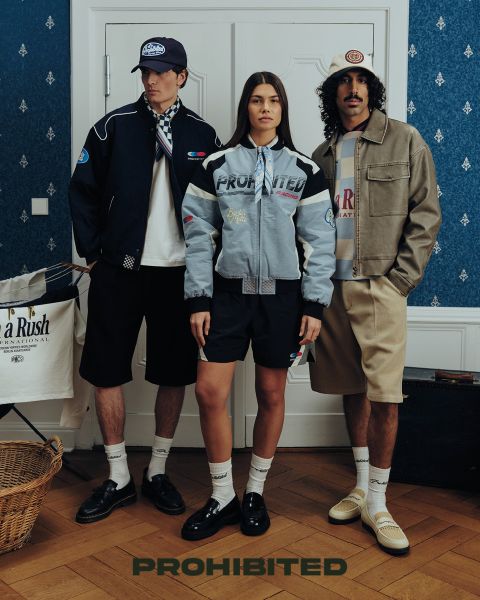 Zwei Männer sitzen auf einem Holzdeck im hohen Gras und spielen Backgammon. Der eine trägt eine rote Mütze, ein kariertes Hemd und Jeans, der andere eine kastanienbraune Mütze, eine olivfarbene Jacke und eine dunkle Hose. Über ihnen steht "PROHIBITED" geschrieben.