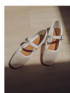 Ein Paar weiße Mary-Jane-Schuhe mit Netzstruktur und Schnallenriemen, auf einem hellen Holzboden platziert, wobei das Sonnenlicht sanfte Schatten wirft.