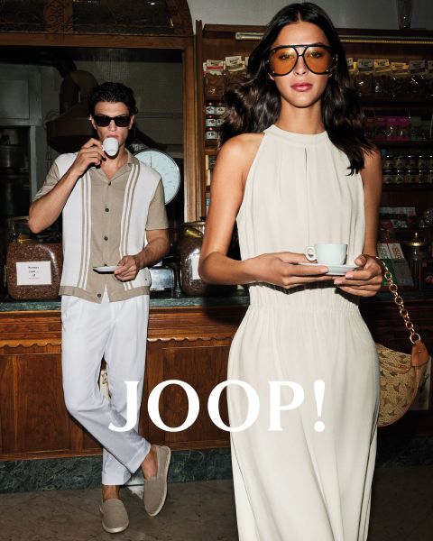 Mann und Frau in stylischer Sommerkleidung in einem Café. Der Mann trägt ein beiges Hemd und hält eine Tasse, während die Frau im hellen Kleid eine Untertasse hält. Beide tragen Sonnenbrillen. „JOOP!“ steht deutlich zu sehen.