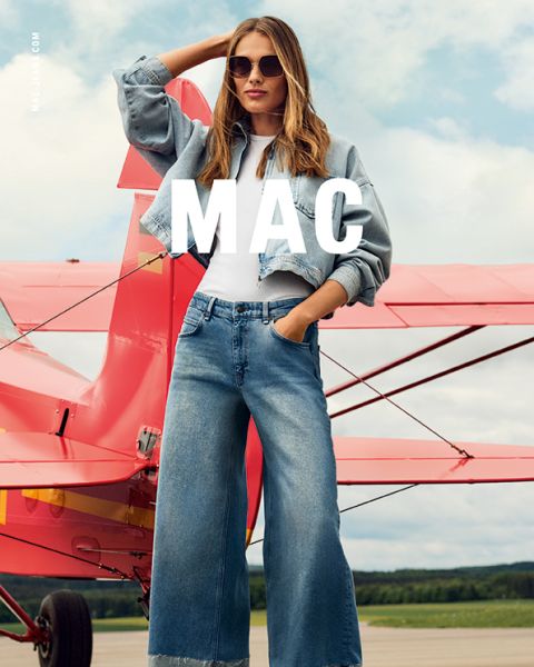 Eine Person mit Sonnenbrille und Jeanskleidung steht an einem klaren Tag selbstbewusst vor einem roten Doppeldecker. Der Text „MAC“ ist in weißer Schrift deutlich über das Bild zu sehen.