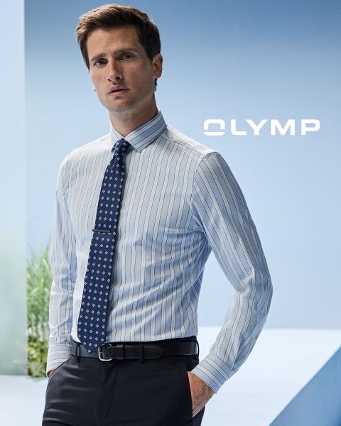 Ein Mann steht selbstbewusst da und trägt ein blau-weiß gestreiftes Hemd mit gemusterter Krawatte und dunkler Hose. Der Hintergrund ist hellblau und das Wort „OLYMP“ ist sichtbar.