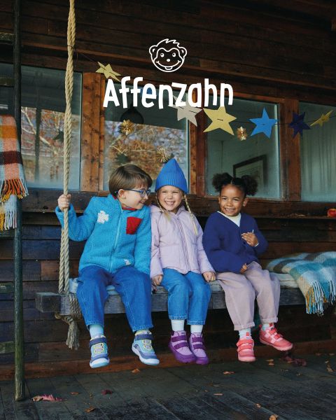 Ein Kind in einem leuchtend orangefarbenen Pullover und gestreiften Hosen sitzt auf einer bunten Fläche und zeigt auf ein Papierflugzeug im Comic-Stil am Himmel. Es lächelt und ist von flauschigen Wolken umgeben. In der Ecke steht „Affenzahn“.