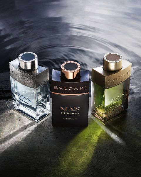 Eine Frau in einem weißen Kleid lehnt sich vor einer modernen Architekturkulisse unter blauem Himmel zurück. Im Vordergrund stehen zwei Flakons des Parfums Bvlgari Omnia Crystalline, die klare und bernsteinfarbene Farbtöne aufweisen.