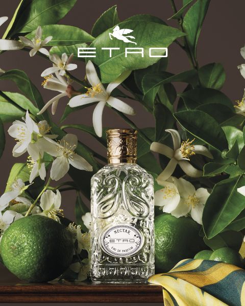 Parfümflakon mit der Aufschrift „ETRO“ und einem Tannenzapfen-Design, umgeben von künstlerischem Dekor: eine Kugel, ein Ei mit einem Schmetterling, ein Stein, ein Blatt, Walnüsse, ein goldener Apfel und eine geformte Hand. Oben das ETRO-Logo vor einem Hintergrund aus blauem Himmel und Meer.