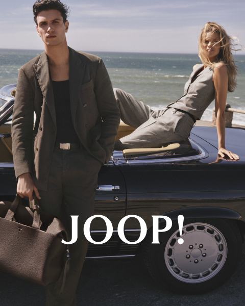 Mann und Frau in stylischer Sommerkleidung in einem Café. Der Mann trägt ein beiges Hemd und hält eine Tasse, während die Frau im hellen Kleid eine Untertasse hält. Beide tragen Sonnenbrillen. „JOOP!“ steht deutlich zu sehen.