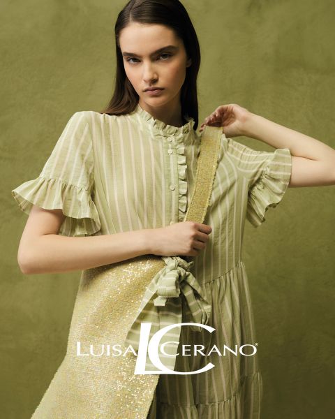 Eine Frau mit langen braunen Haaren trägt ein geblümtes Kleid und ein strukturiertes, rostfarbenes Pelzgewand über der Schulter. Sie blickt direkt in die Kamera. Unten in der Mitte ist der Text „Luisa Cerano“ zu sehen.