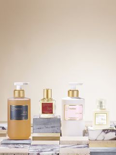 Drei Parfüme auf einer Marmoroberfläche: eine Pumpflasche mit der Aufschrift „OUD“, eine kleinere quadratische Flasche mit goldenem Verschluss und eine weiße Pumpflasche mit der Aufschrift „À la rose“. Der Hintergrund ist in sanftem Beige gehalten.