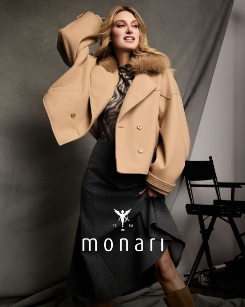 Eine Frau in einem Cape aus Kunstfell über einem Oberteil mit Leopardenmuster und einem braunen Rock sitzt und posiert; unten sind „monari“ und das Logo zu sehen.