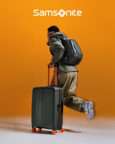 Hellgrüner Samsonite-Koffer mit strukturiertem Muster und vier Rollen. Der Griff ist ausziehbar. Das große „Samsonite“-Logo ist quer über den Koffer gebreitet. Der Hintergrund hat ein wellenförmiges grün-weißes Design.