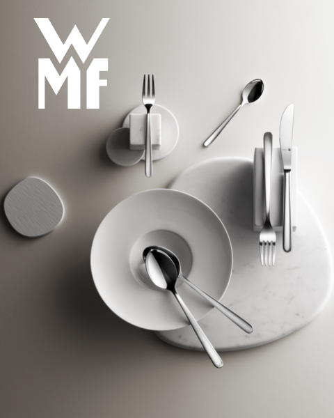 Ein mit Feigen, Brombeeren und aromatischen Garnituren gefüllter Kochtopf steht auf einem dunklen Holzbrett. Über dem Kochtopf ist das WMF-Logo zu sehen. Der Hintergrund ist eine strukturierte dunkle Oberfläche.
