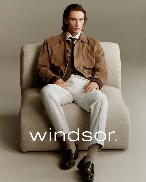 Ein Mann in einem braunen Mantel und eine Frau in einem cremefarbenen Mantel und Schal stehen im Freien mit Bergen im Hintergrund. Das Wort "windsor." ist am unteren Rand des Bildes zu lesen.