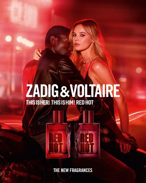 Frau mit langen roten Haaren und schwarzem Outfit sitzt auf einem Bett in einem Zimmer mit Vogelkäfig und großem Fenster. Text: „Zadig & Voltaire“ und „Zadig: Der neue nachfüllbare Duft“. Logo mit Flügeln und einem Hufeisen.