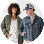 Eine Frau mit lockigem Haar, einem grünen Mantel und einem weißen Hemd steht neben einem Mann in blauer Jeansjacke, beigem Hemd und Mütze. Beide modellieren neutrale Gesichtsausdrücke vor einem schlichten Hintergrund.