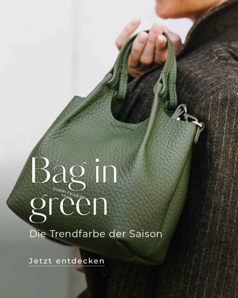Eine Person hält eine grüne, strukturierte Handtasche mit kurzen Henkeln. Der überlagerte Text lautet "Bag in green-Die Trendfarbe der Saison. Jetzt entdecken." Die Person trägt einen braunen Mantel und nur ihre Hand und ein Teil ihres Mantels sind sichtbar.