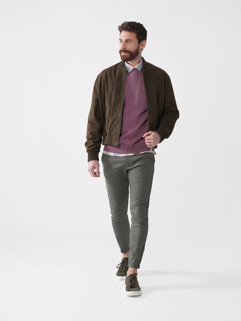 Ein Mann mit Bart geht. Er trägt eine braune Jacke, einen rosa Pullover, ein weißes Hemd, eine graue Hose und grüne Turnschuhe. Der Hintergrund ist schlicht weiß.