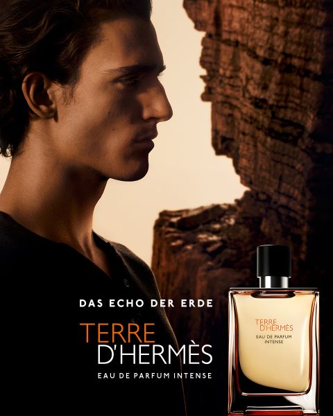 Seitenprofil einer Person mit langen Haaren vor einem felsigen Hintergrund. Im Vordergrund ist die Vorderansicht einer Flasche Terre D'Hermès Eau de Parfum Intense zu sehen. Der Text lautet: „Das Echo der Erde.“.