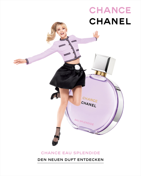 Eine Frau in einem stylischen schwarz-lavendelfarbenen Outfit posiert fröhlich neben einer großen Flasche Chanel Chance Eau Splendide. Die Anzeige enthält einen deutschen Text, der den neuen Duft hervorhebt.
