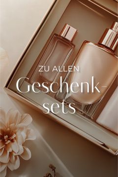 Eine Geschenkbox mit drei eleganten Parfüm- und Kosmetikflakons in Beige- und Goldtönen und dekorativen Blumen in der Ecke. Der deutsche Text lautet: „Zu allen Geschenksets.“.