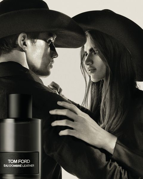 Ein Mann und eine Frau mit breitkrempigen Hüten stehen sich mit angespanntem Gesichtsausdruck gegenüber. Im Vordergrund steht eine Flasche Eau d'Ombré Leather von Tom Ford. Das Bild ist in Schwarzweiß gehalten und vermittelt einen dramatischen, klassischen Eindruck.