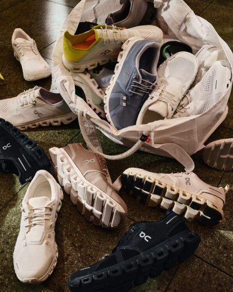 Eine Vielzahl von On-Laufschuhen in verschiedenen Farben liegt auf dem Boden verstreut und quillt aus einer weißen Tragetasche hervor, die ihre unverwechselbaren gepolsterten Sohlen zur Schau stellt.