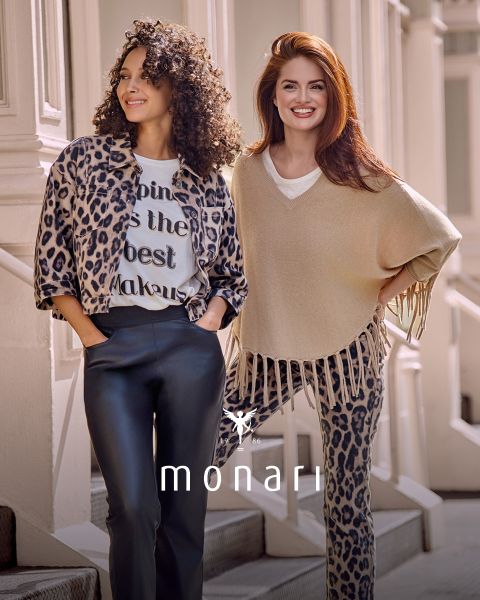 Zwei Frauen stehen in stylischen Outfits im Freien. Die eine trägt eine Jacke mit Leopardenmuster und eine schwarze Hose, die andere einen beigen Fransenpullover und eine Hose mit Leopardenmuster. Beide lächeln. Unten ist das Monari-Markenlogo zu sehen.