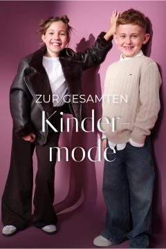 Zwei lächelnde Kinder stehen vor einer lila Wand. Das Mädchen trägt eine schwarze Jacke, ein weißes Oberteil und eine weit geschnittene Hose. Der Junge trägt einen cremefarbenen Pullover und Jeans. Der weiße deutsche Text lautet: "Zur gesamten Kindermode.